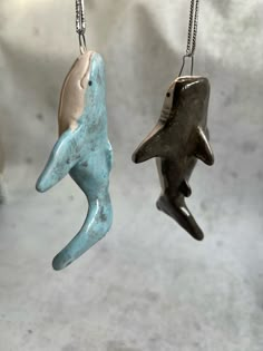 two ceramic dolphins hanging from chains on a white surface, one is blue and the other is brown