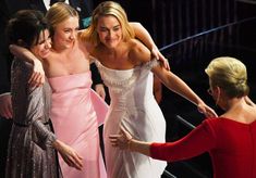 three women in dresses hugging each other on the oscars red carpet