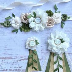 three paper flowers and ribbons on a white wooden surface with ribbon around them, one is green and the other is gold