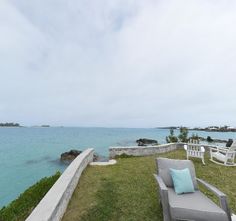 a lawn chair sitting on top of a lush green field next to the ocean with blue water