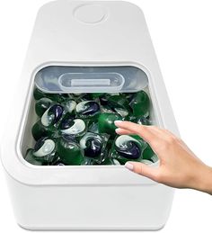 a hand is reaching for some green and white marbles in a bin that's on top of a table