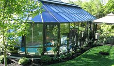 a glass house sitting in the middle of a lush green yard next to a tree