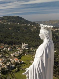 there is a statue that looks like jesus in the middle of a field with buildings and hills behind it