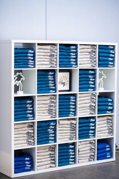 a white bookcase filled with lots of blue and white folded shirts on top of each other