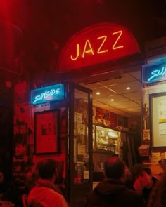 people are sitting at tables in front of a jazz bar with neon signs on the doors