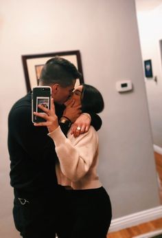 a man and woman kissing in front of a mirror with their cell phones up to their faces