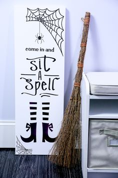 a broom sitting next to a sign that says come in and sit at spell