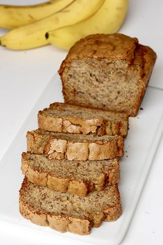 sliced banana bread sitting on top of a white cutting board next to two ripe bananas