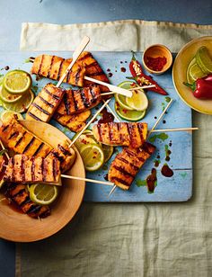 grilled chicken skewers on a platter with limes and chilies