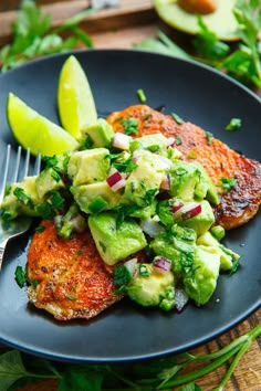 a black plate topped with meat covered in guacamole and lime wedges