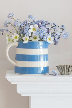 a blue and white striped vase with flowers in it sitting on a shelf next to seashells