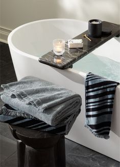 a white bath tub sitting next to a wooden stool and candle on top of it