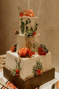 a three tiered cake with orange flowers and cactus decorations on the top is sitting on a table