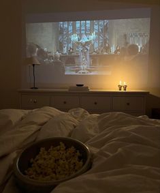 a bowl of popcorn sitting on top of a bed in front of a tv screen