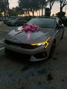 a gray car with a pink bow on it's hood parked in a parking lot