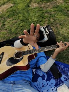 a man sitting in the grass with his hand up and holding an acoustic guitar to his face