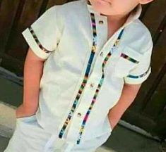 a young boy wearing a white shirt and blue jeans standing in front of a wooden door