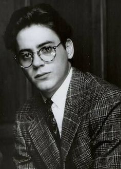 a black and white photo of a young man wearing glasses with a suit jacket on