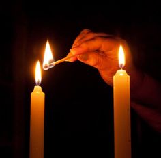 someone lighting candles in the dark with one hand holding a lighter and another is pointing at them