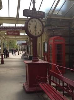 a red bench sitting next to a clock in a train station