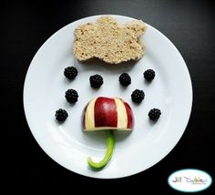 a white plate topped with an apple and blackberries next to a piece of bread