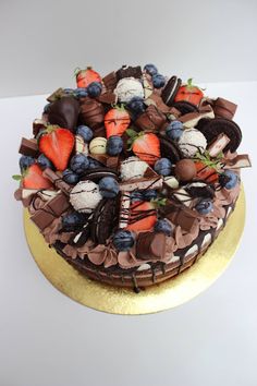 a chocolate cake topped with strawberries, blueberries and other toppings on a gold platter