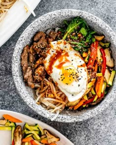 two bowls filled with different types of food on top of a marble table next to chopsticks