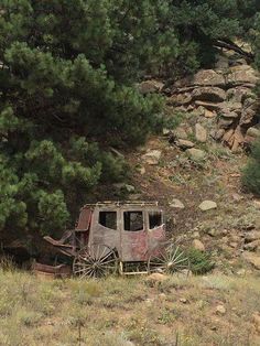 an old, rusted wagon sits on the side of a hill near some trees