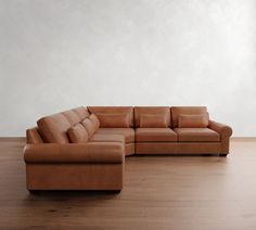 a brown leather couch sitting on top of a wooden floor next to a white wall