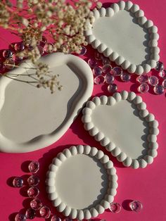 three white heart shaped plates sitting on top of a pink table