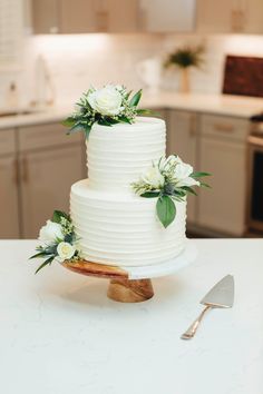 a white wedding cake sitting on top of a counter next to a knife and fork