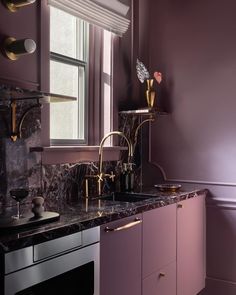 a kitchen with purple walls and marble counter tops, gold faucets on the sink