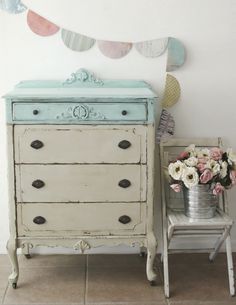 an old dresser with flowers on it next to a small chair and bunting flags