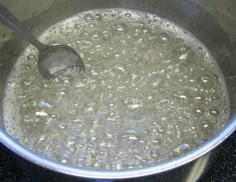 a pot full of water with a ladle in the bottom, on top of a stove