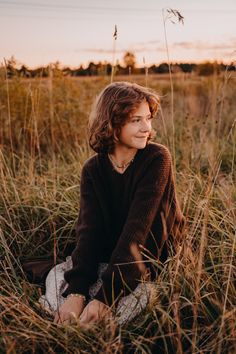 a woman sitting in tall grass with her head turned to the side and looking off into the distance