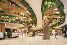 the inside of a shopping mall with people walking around and trees growing on the ceiling