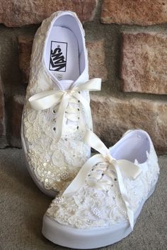 a pair of white shoes with lace and bows on the side, against a brick wall