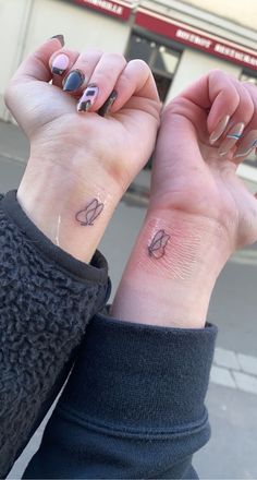 two people with matching tattoos on their wrists holding each other's hands in front of a building