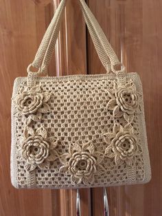 a crocheted purse hanging from a hook on a wooden door with metal handles