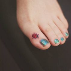 a ladybug tattoo on the foot of a person with blue and green nail polish