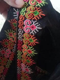 someone is stitching something on the back of a jacket with colorful threadwork and beads