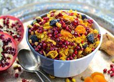 a bowl filled with fruit and nuts next to two spoons on top of a table