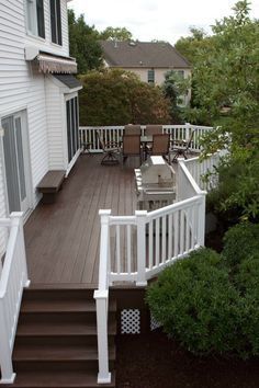 a deck with chairs, table and grill on it in front of a white house