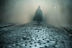 a man standing on a cobblestone road in the dark with fog coming from behind him