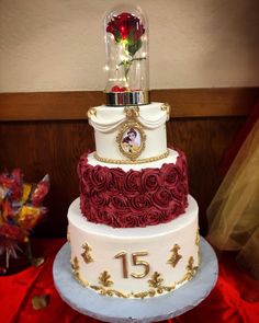 a three tiered wedding cake with roses on top and the number fifteen in gold