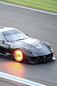 a black sports car driving down a race track with its lights on and the front wheels spinning