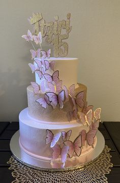 a three tiered cake with pink butterflies on the top and gold numbers on the bottom