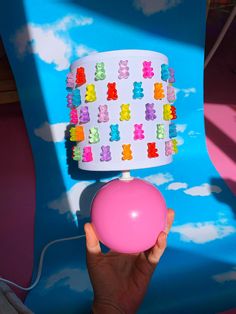 a person holding a pink ball in front of a colorful cake on top of a blue chair