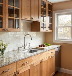 a kitchen with wooden cabinets and marble counter tops, along with a window over the sink