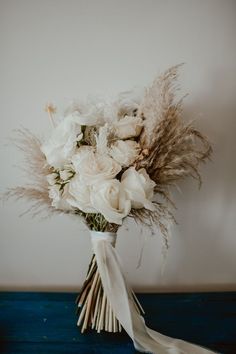 a bouquet of white flowers and feathers on a blue table with a white wall in the background